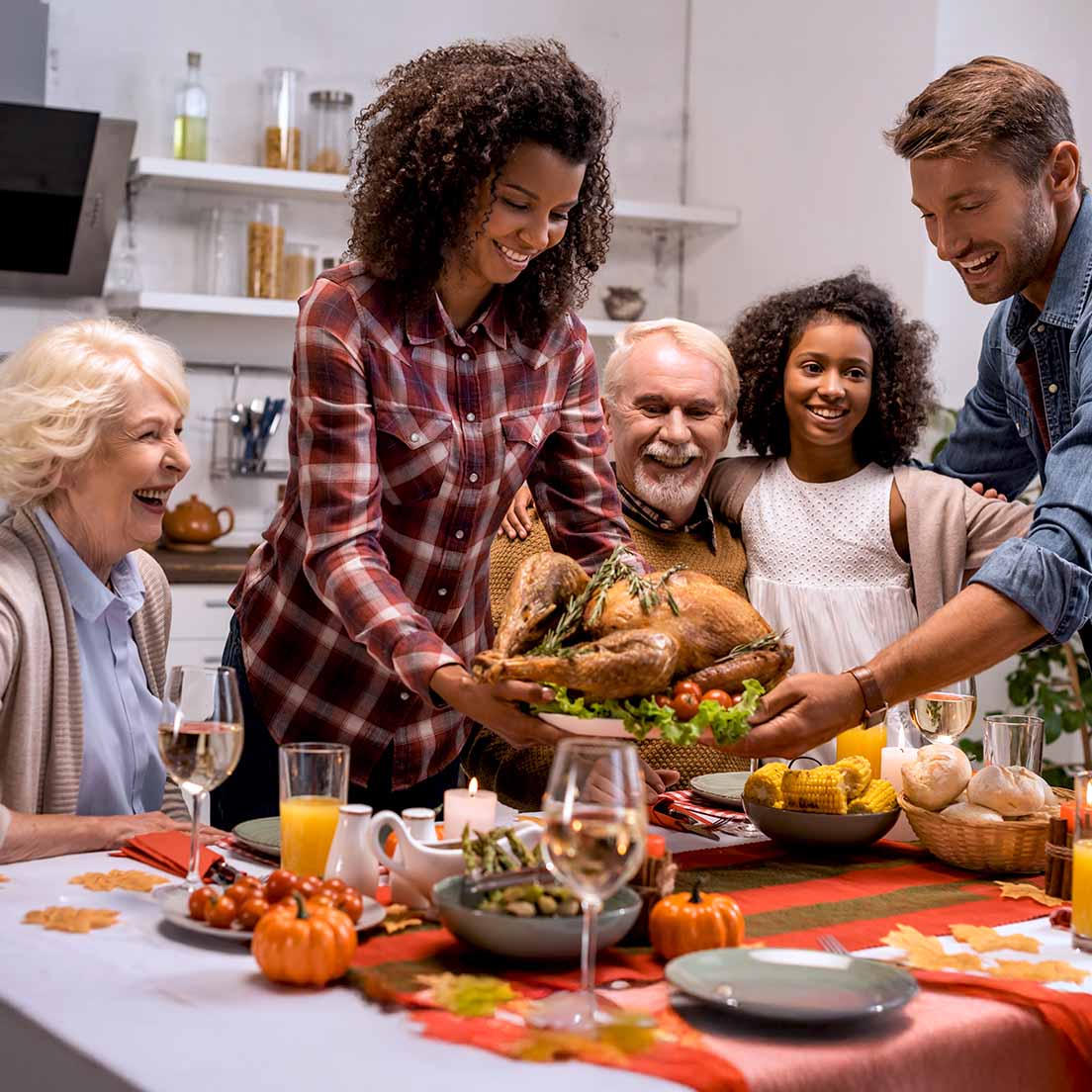 Family sets a roasted turkey on a festive Thanksgiving table, smiling together